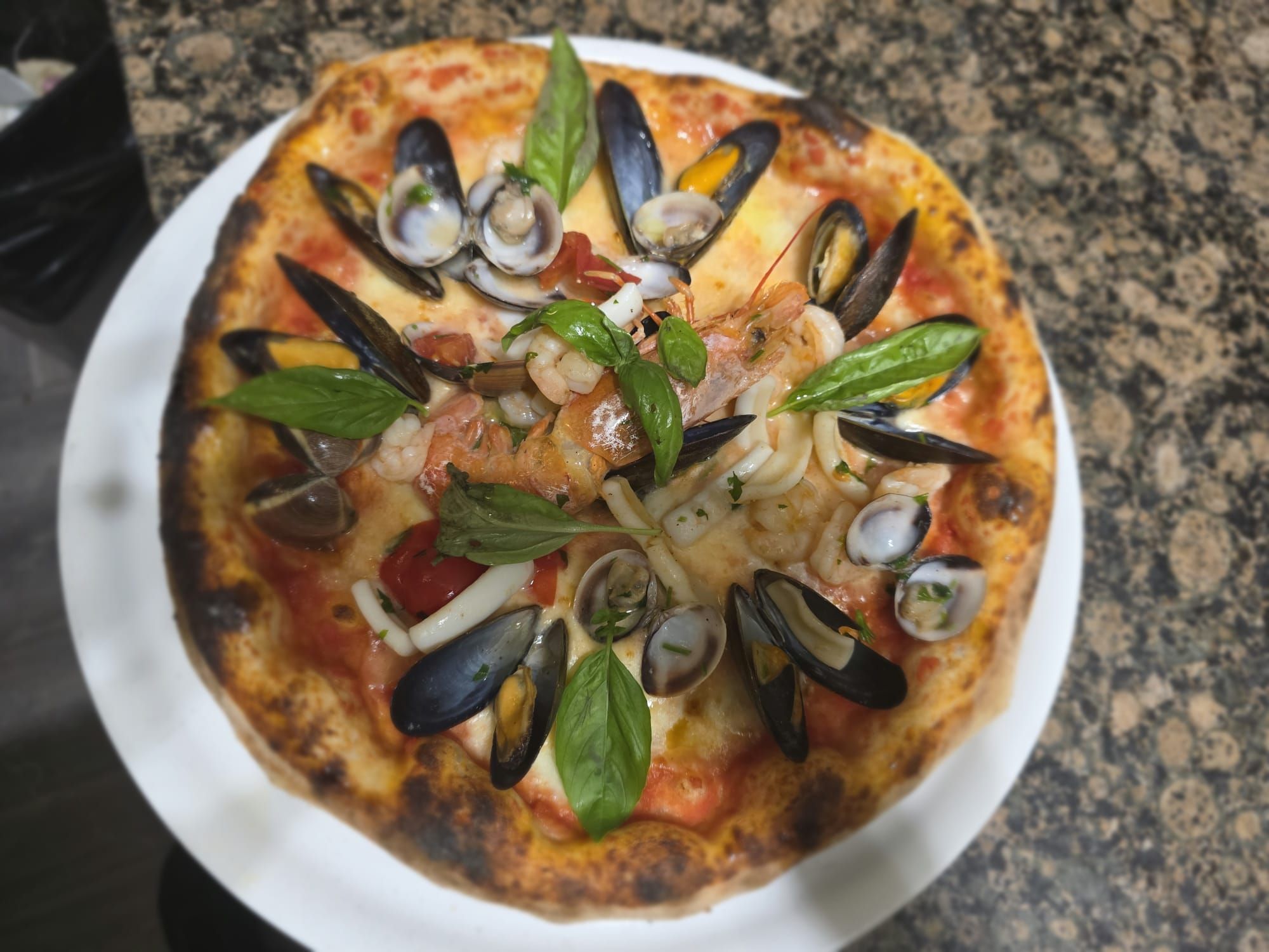 Pizza ai frutti di mare con cozze, vongole e basilico, vista dall’alto
