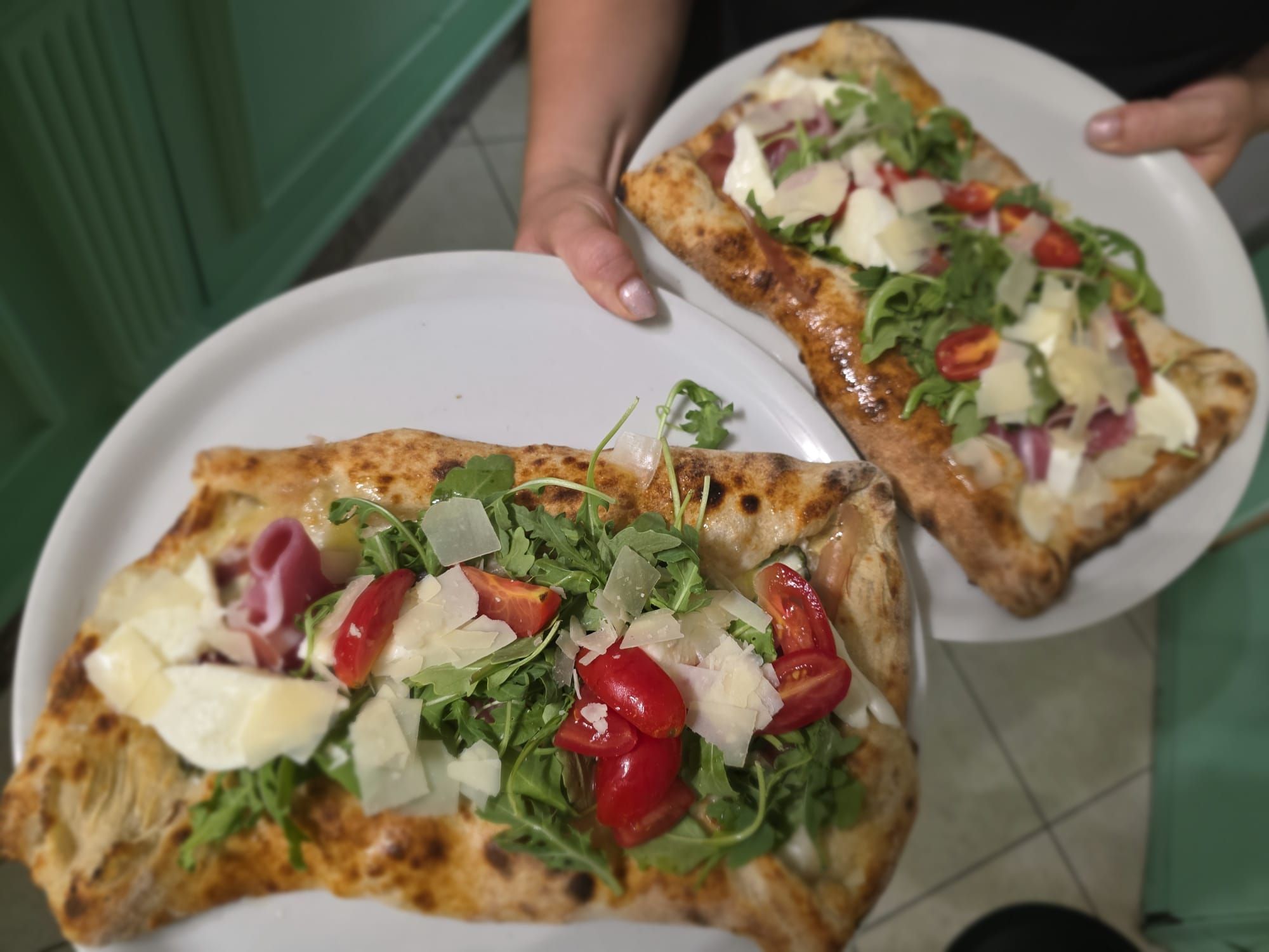 Due pizze in pala con rucola, pomodorini, scaglie di grana e salumi, servite al tavolo
